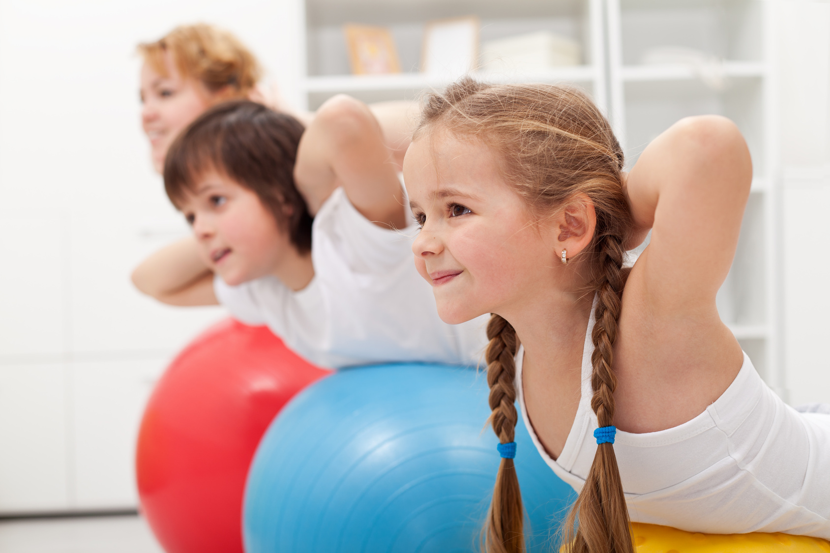 Kids and woman doing gymnastic exercises with balls - stretching their back